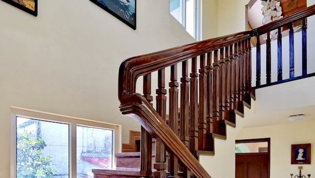 Una imponente escalera de madera con balaustres y barandilla, que conduce a un rellano con una puerta y un candelabro.