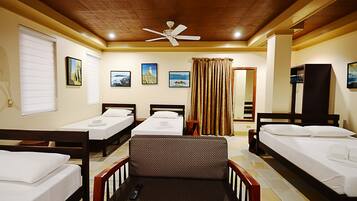 A hotel room with three single beds, a sofa, a ceiling fan, and a window with blinds.