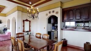 Un comedor con mesa y sillas de madera, una araña y una zona de cocina con armarios y un lavamanos.