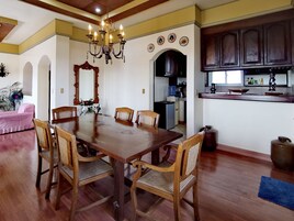 A dining area with a wooden table and chairs, a chandelier, and a kitchen area with cabinets and a sink.