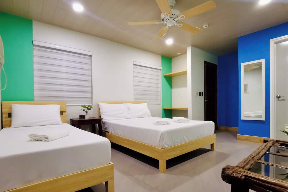 A hotel room with two beds, a ceiling fan, a mirror, and a small table.