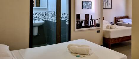 Habitación de hotel con cama, baño con lavamanos y espejo, y zona de comedor con sillas y mesa.