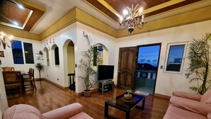 Amplia sala de estar con piso de madera, televisor, sofá y comedor con sillas y mesa.