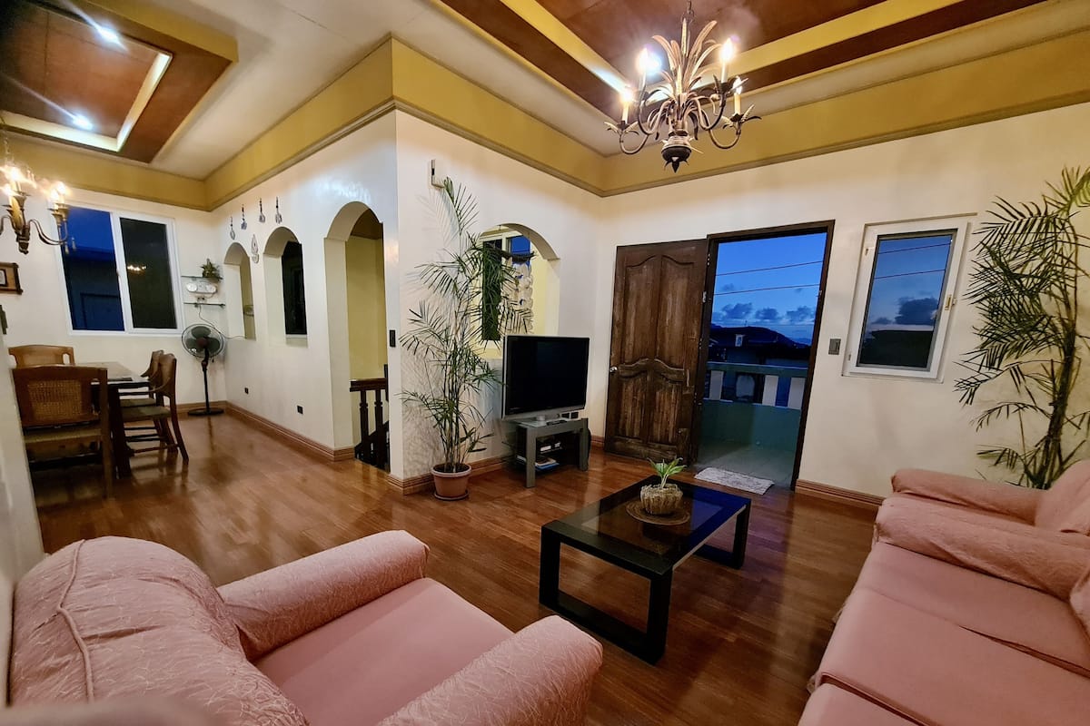 A spacious living room with a wooden floor, a television, a sofa, and a dining area with chairs and a table.