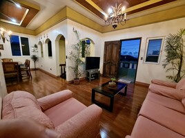 A spacious living room with a wooden floor, a television, a sofa, and a dining area with chairs and a table.