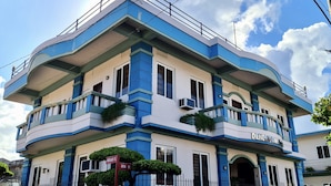 A multi-story building with a blue and white color scheme, featuring balconies with plants, and a sign indicating "DENDRALS HOTEL".