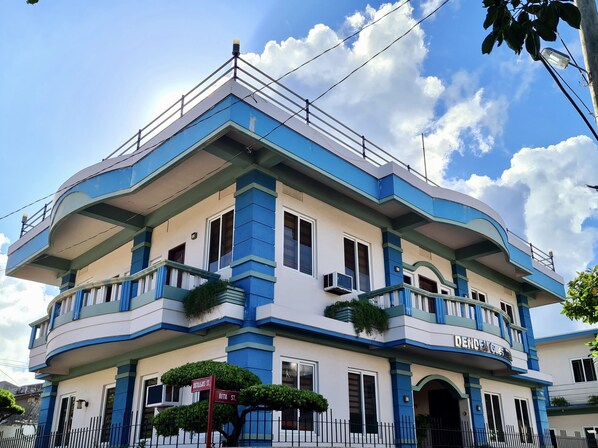 A multi-story building with a blue and white color scheme, featuring balconies with plants, and a sign indicating "DENDRALS HOTEL". - Den Den Guesthouse (Basco)