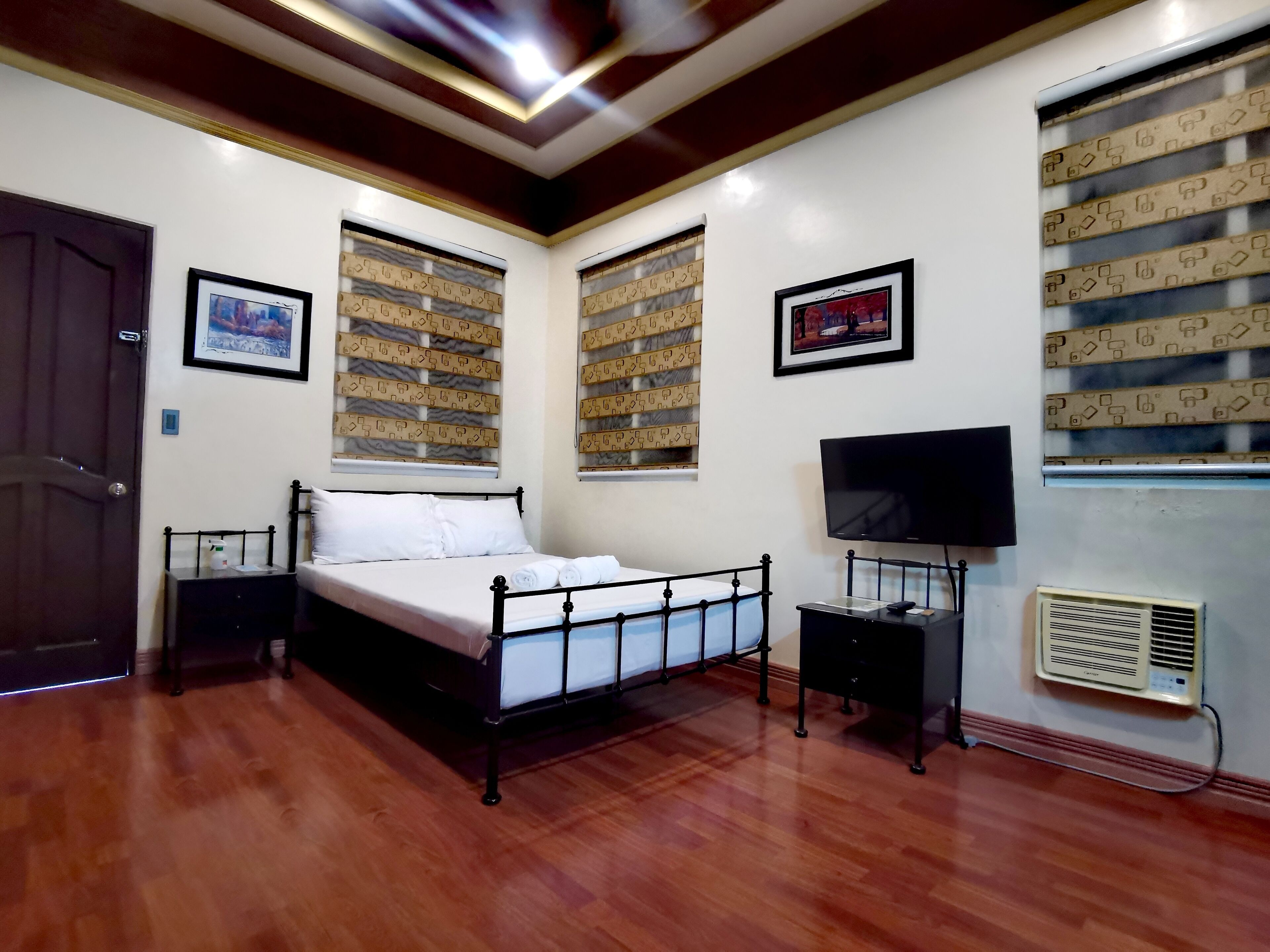 A bedroom with a bed, a TV, a heater, and patterned window treatments.