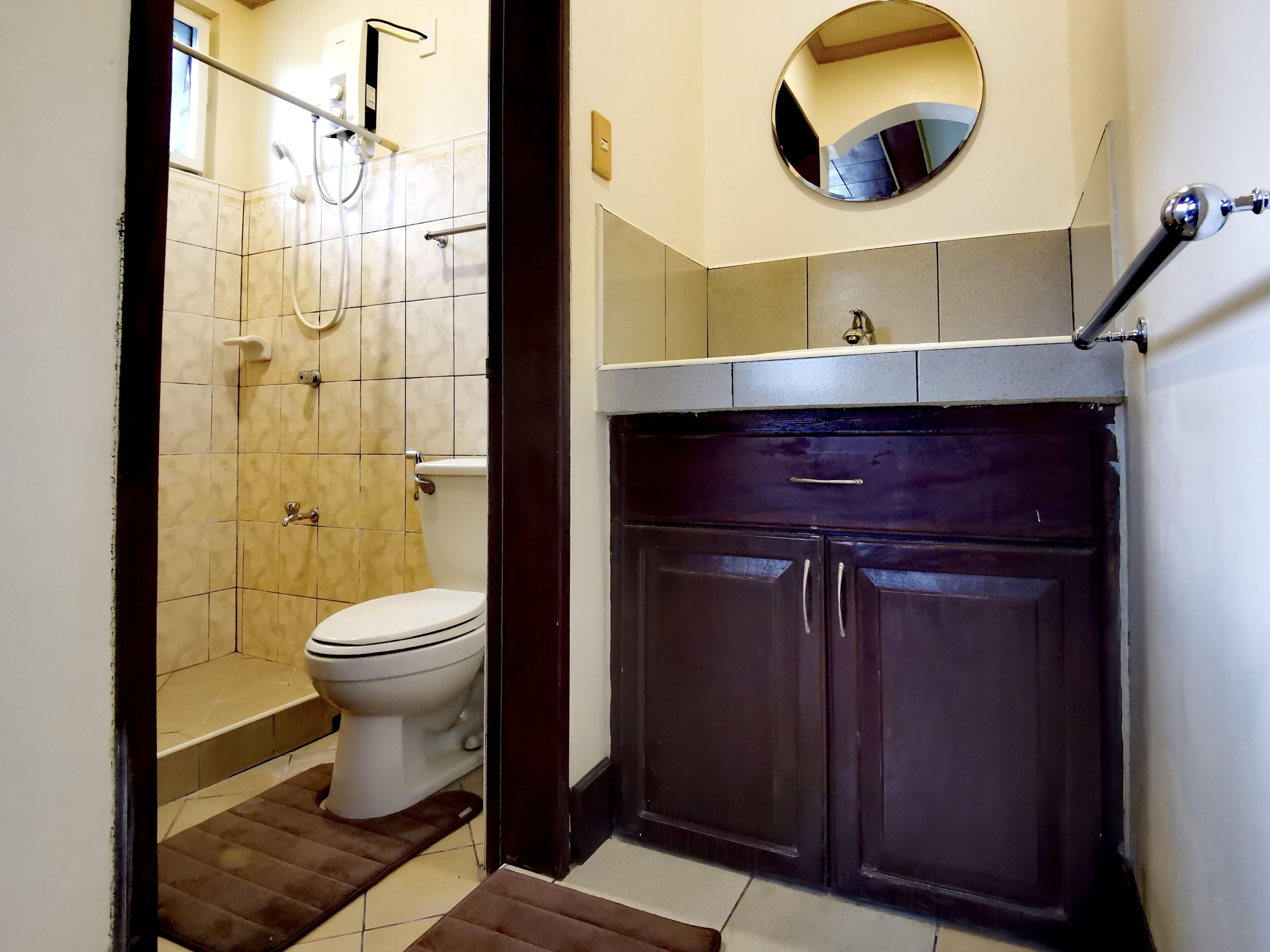 A bathroom with a toilet, shower, and dark wooden cabinets.