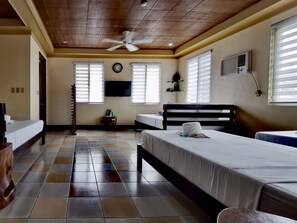 A hotel room with a tiled floor, a ceiling fan, a bed, a bedside table, a TV, and a window with blinds. - Den Den Guesthouse (Basco)