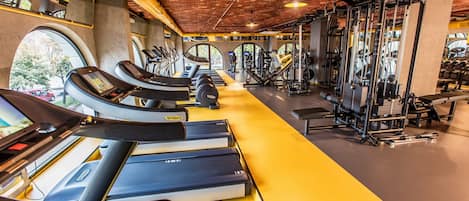 A gym with treadmills, weight machines, and a brick ceiling.