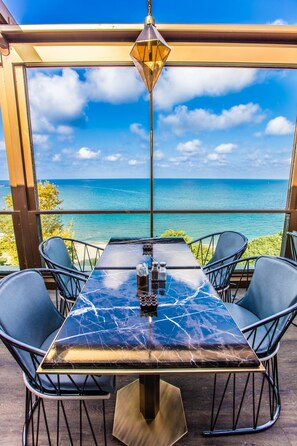 A table with a cracked glass top, four chairs, salt and pepper shakers, and a hanging light fixture.