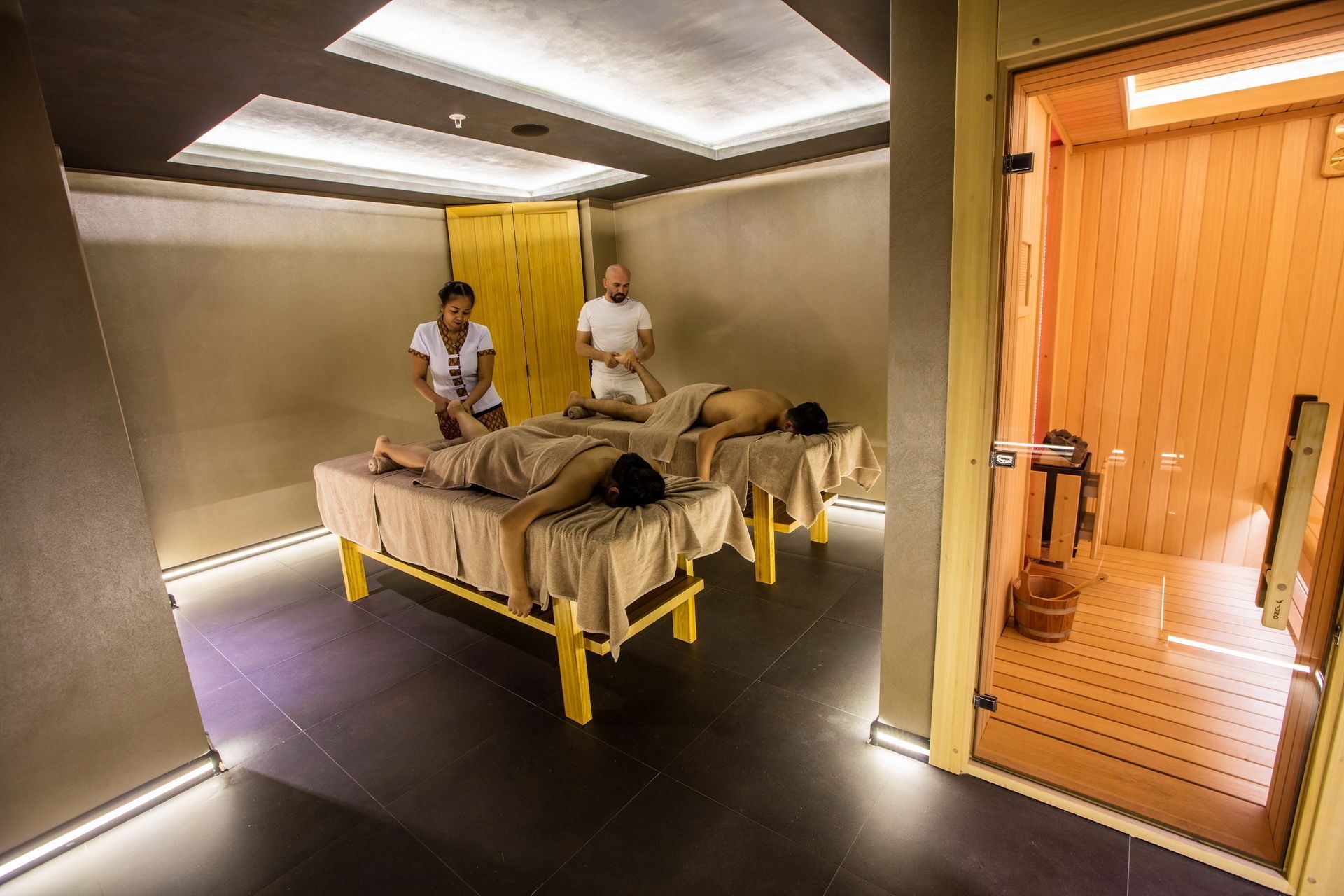 Una stanza per massaggi con tre lettini, una porta in legno e un pavimento piastrellato.