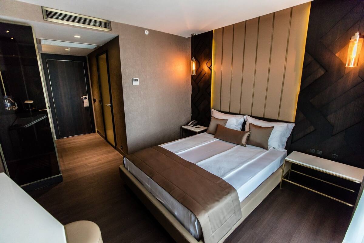 Ein modernes Hotelzimmer mit einem großen Bett, Nachttischen, einem Schreibtisch und einem Kleiderschrank.
