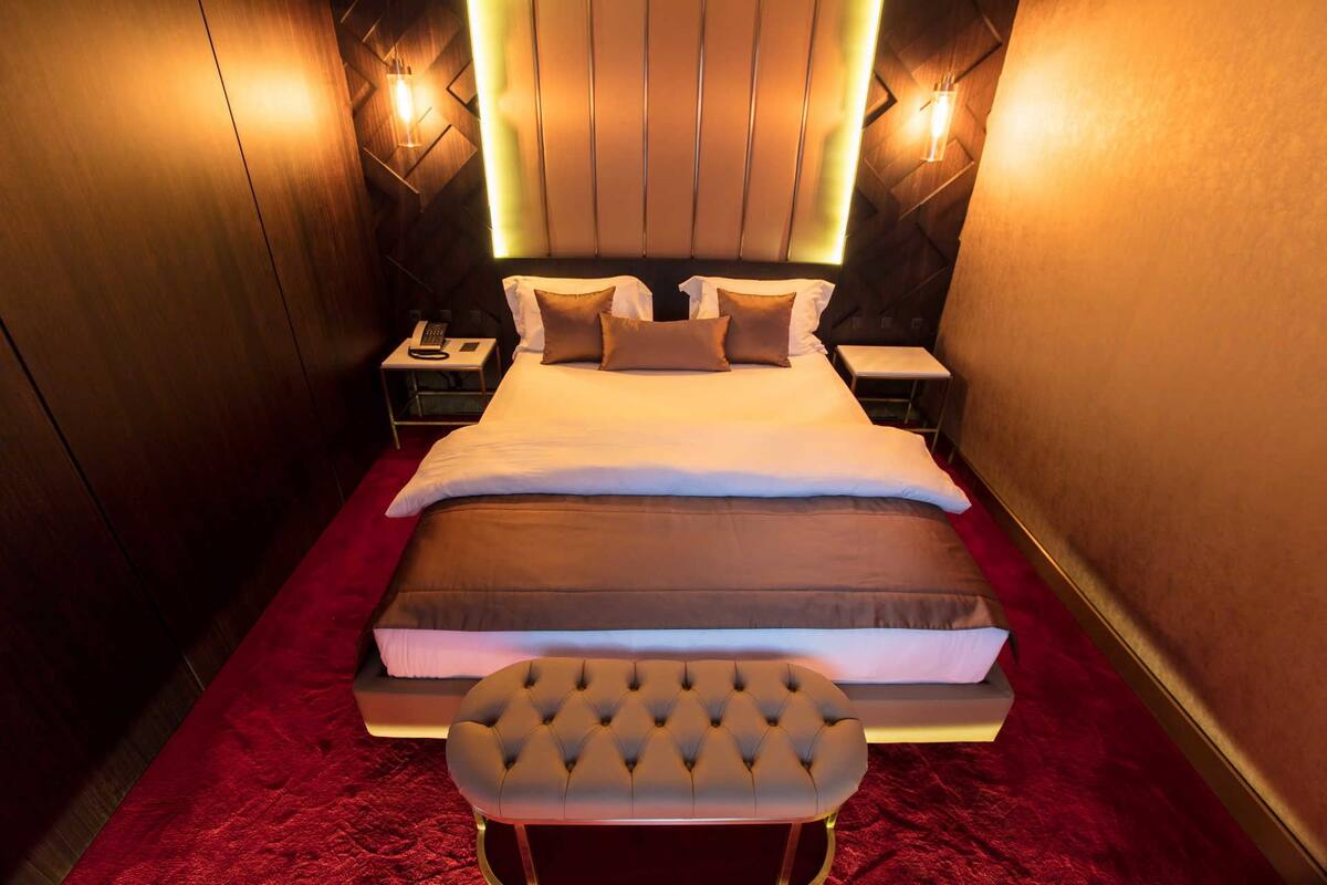 Ein Hotelzimmer mit einem großen Bett, einem Nachttisch mit Telefon und einem roten Teppich.