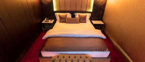Una habitación de hotel con una cama grande, una mesita de noche con un teléfono y una alfombra roja.