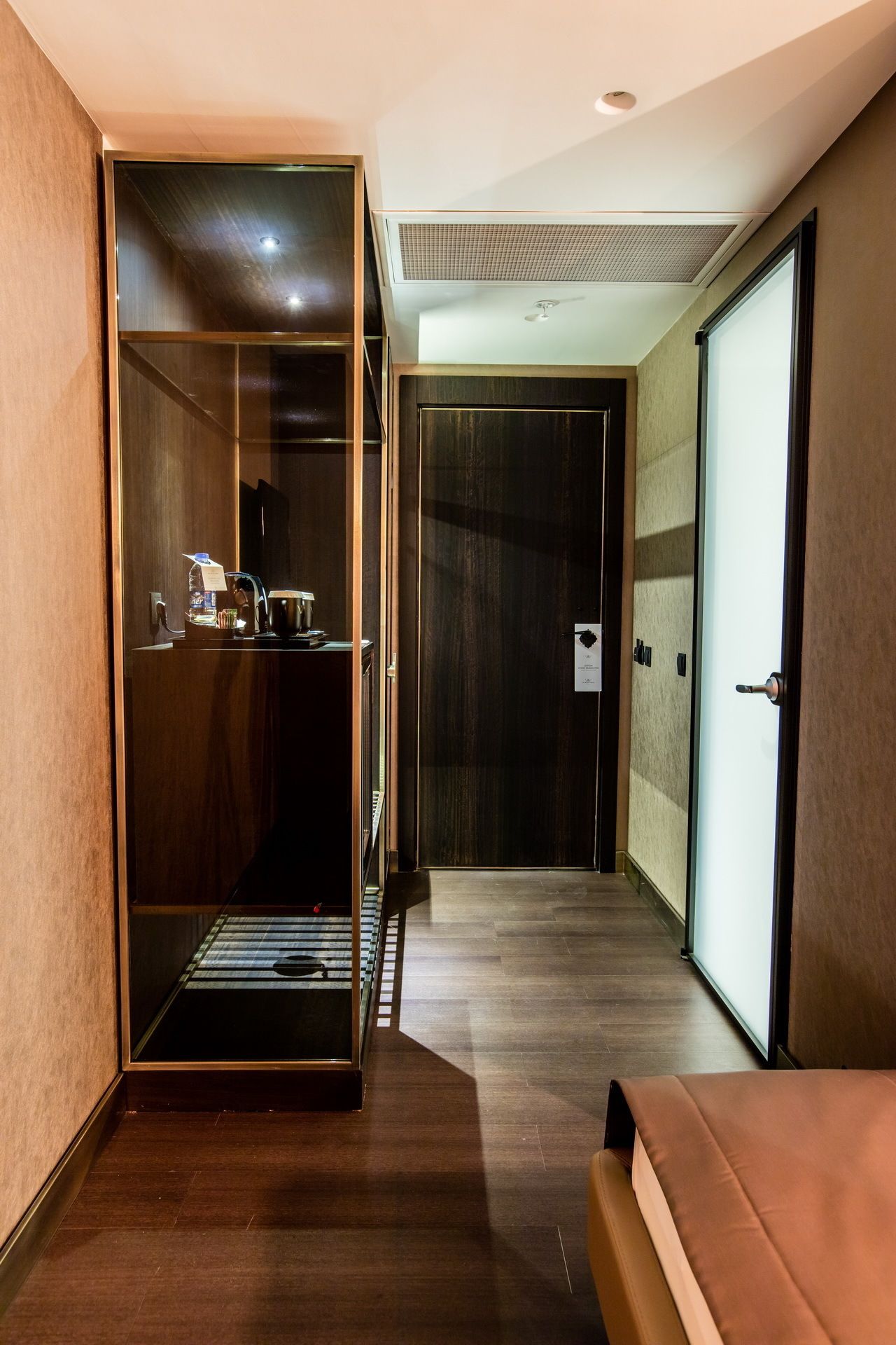 A hotel corridor with a sliding door leading to a room, a bench, and a door with a sign.