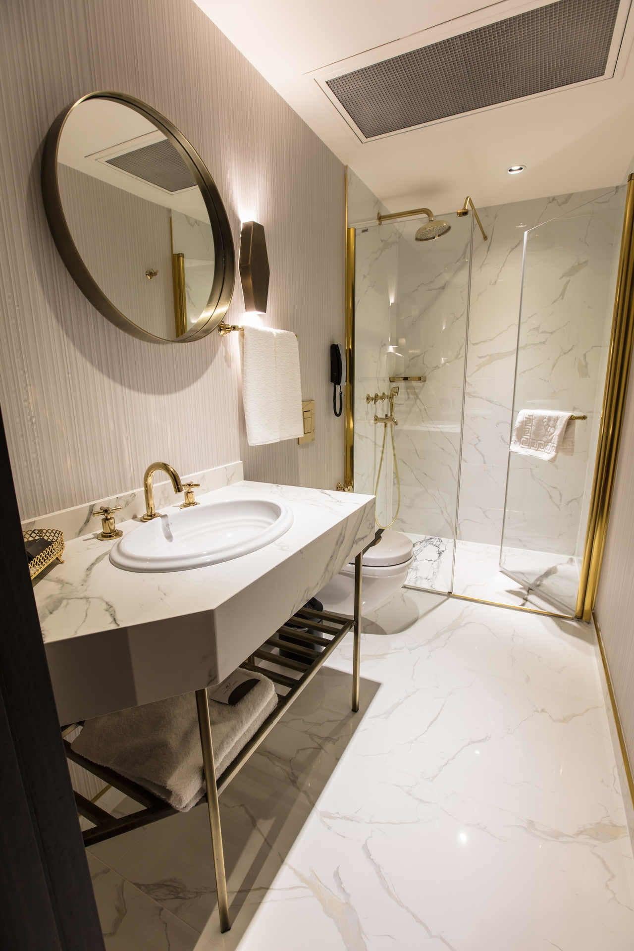 A modern bathroom with a large oval sink, a round mirror, a glass-enclosed shower, and marble flooring.
