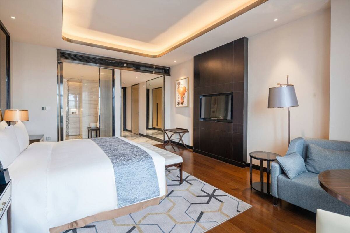 Una habitación de hotel moderna con una cama grande, un sofá, un televisor y una mesita.