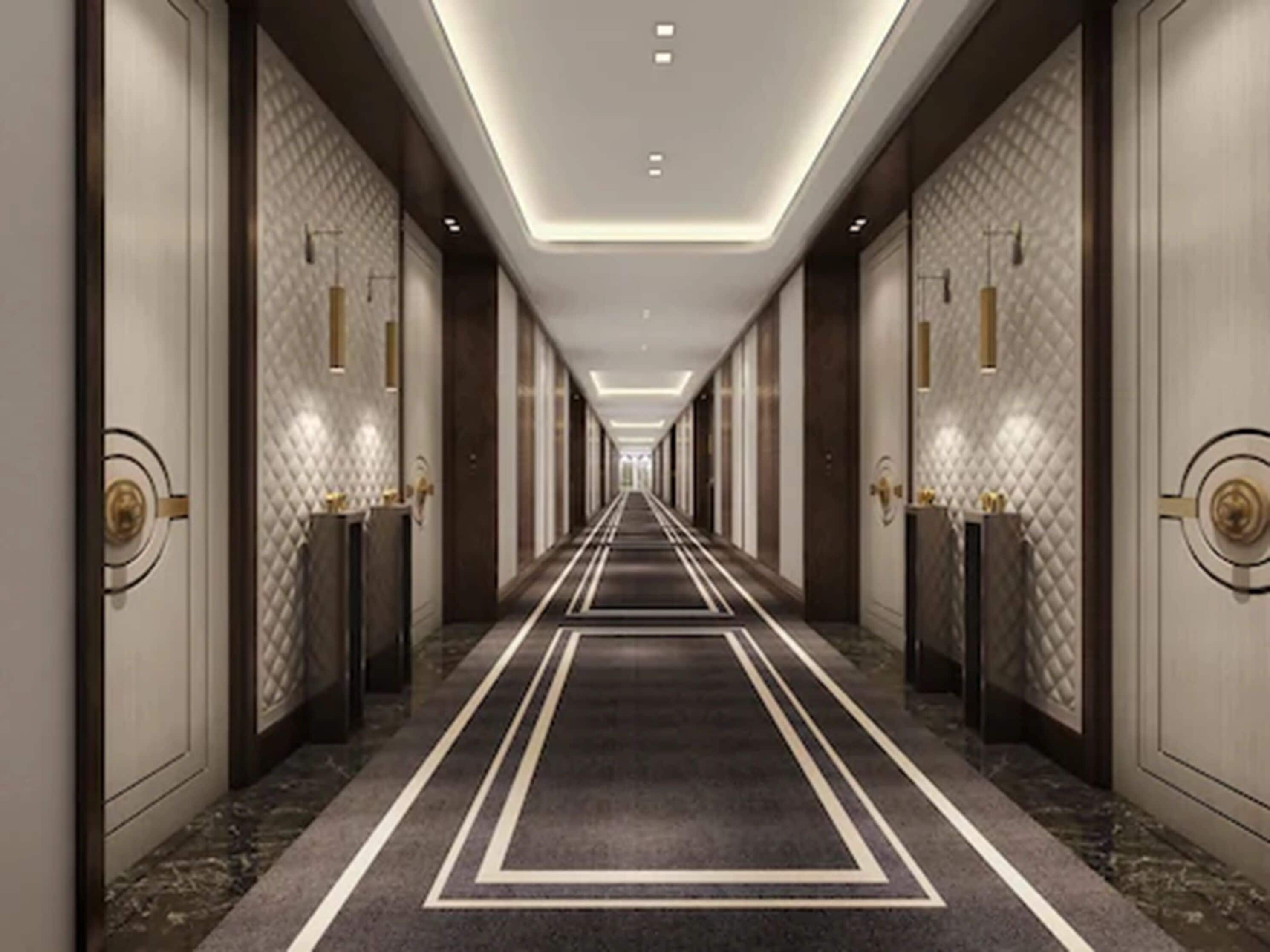 A long, narrow hotel corridor with a patterned carpet, dark floor, and light-colored walls.
