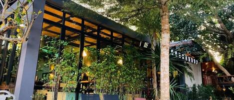 An outdoor seating area with chairs and tables, surrounded by lush greenery and a pergola structure.