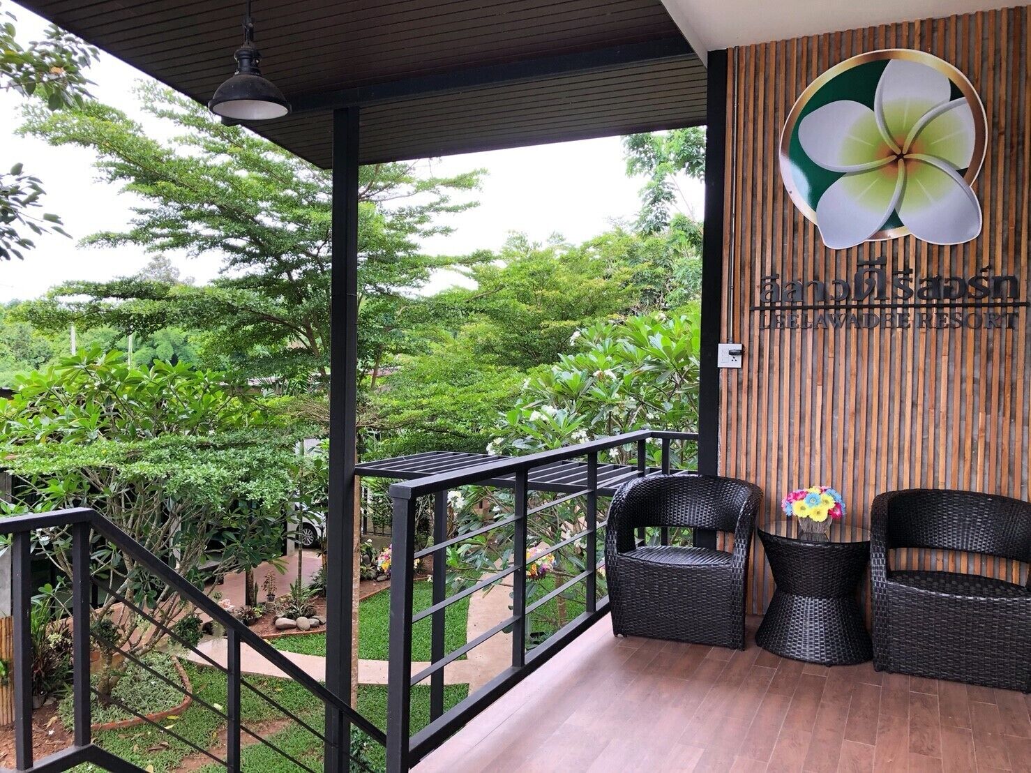 A balcony with wicker chairs, a hanging light fixture, and a wooden wall with a flower design.