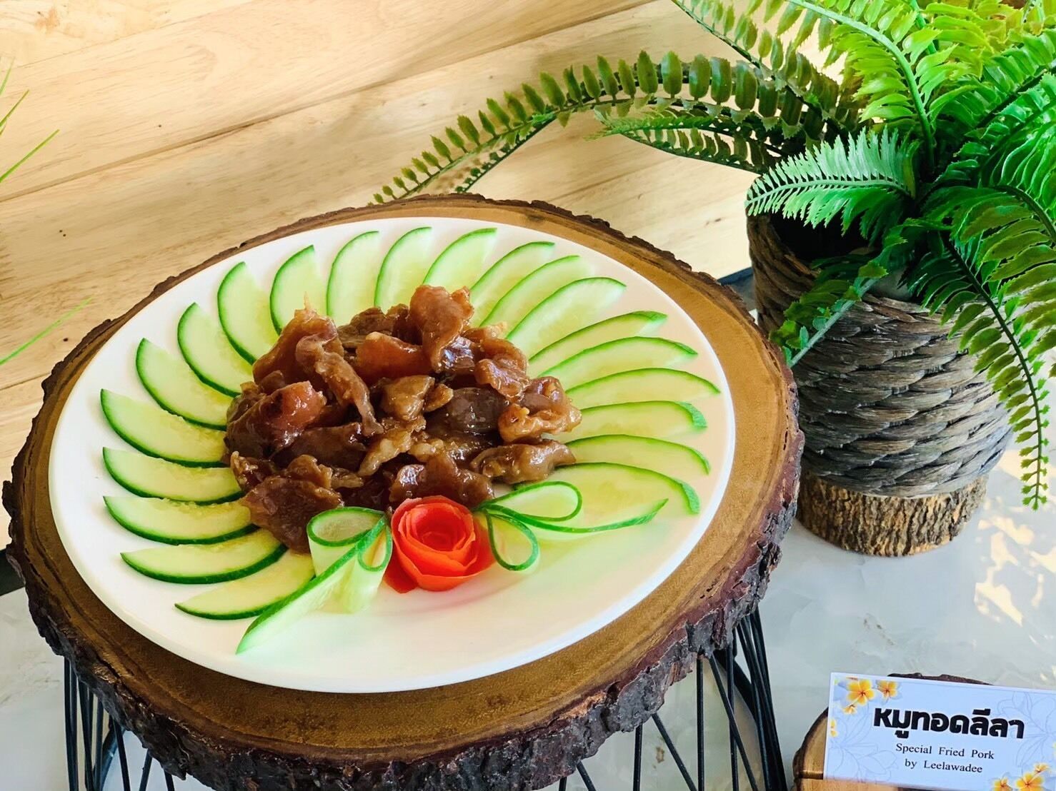 A plate of special fried pork by Leclawadee on a wooden table with a fern plant in the background.