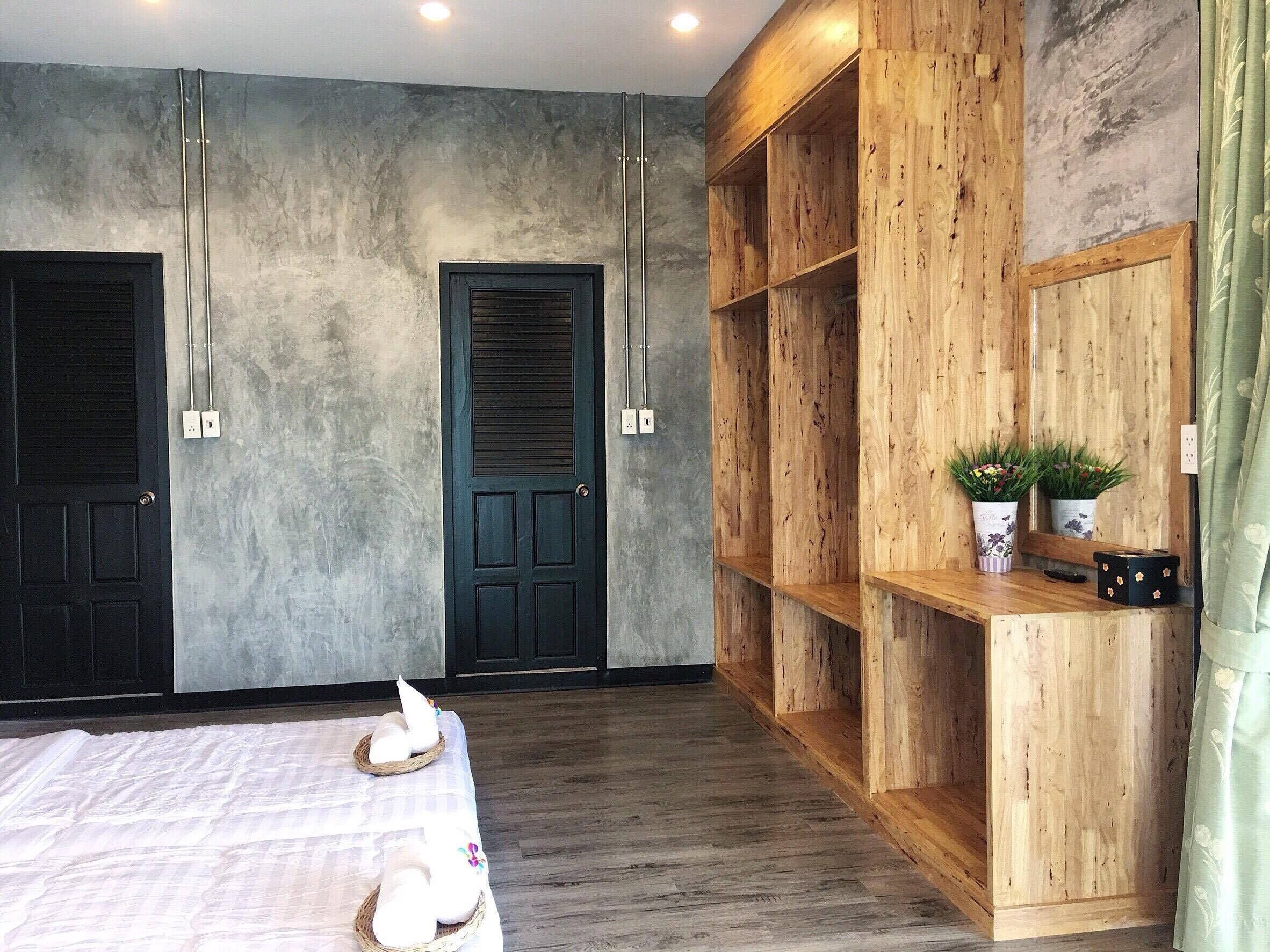 A bedroom with a bed, two doors, a wooden shelving unit, and a small table with plants.