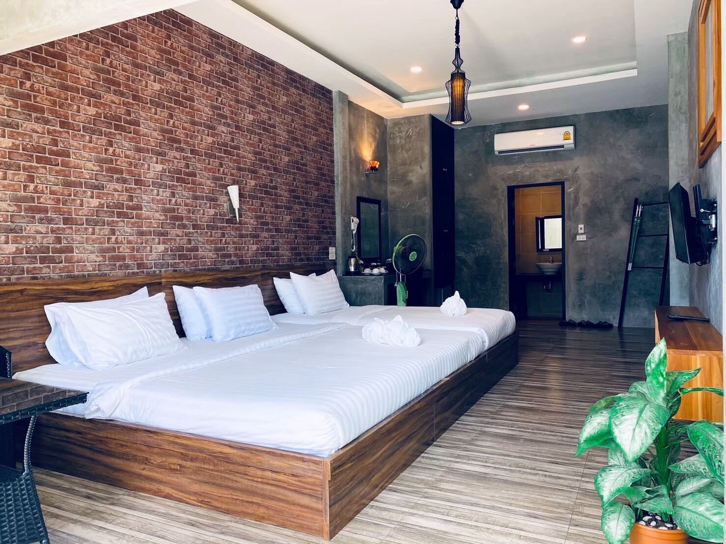 Una camera d'albergo moderna con un letto grande, una parete decorata in mattoni, un pavimento in legno e una pianta in vaso.