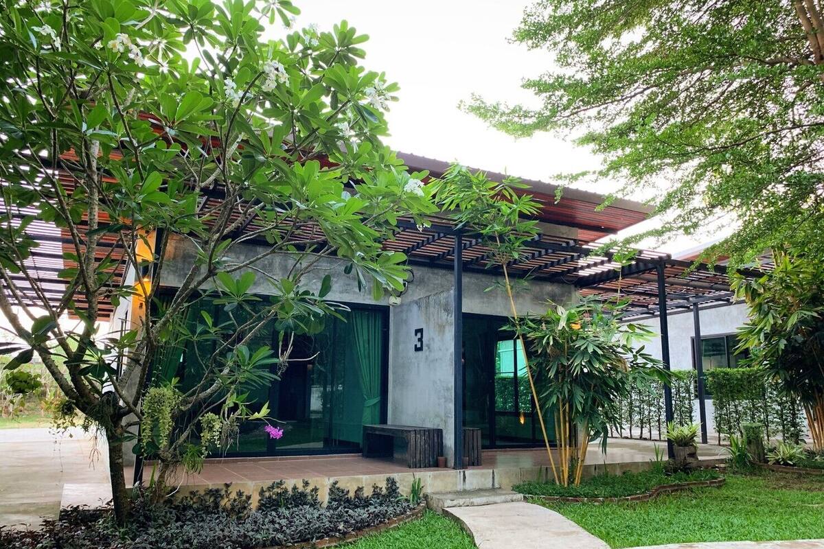 Un bâtiment moderne doté d’une façade en béton, d’une entrée abritée et d’un jardin bien entretenu, agrémenté de diverses plantes et d’un sentier.