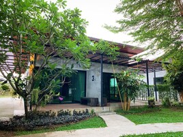 Un edificio moderno con fachada de concreto, un acceso cubierto y un jardín bien cuidado con diversas plantas y un sendero.