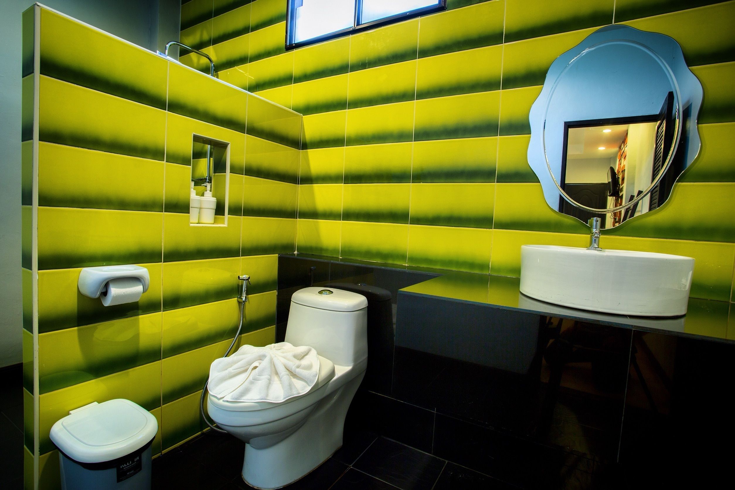 Un baño con baldosas verde a rayas, un inodoro blanco, un lavabo blanco y un espejo.