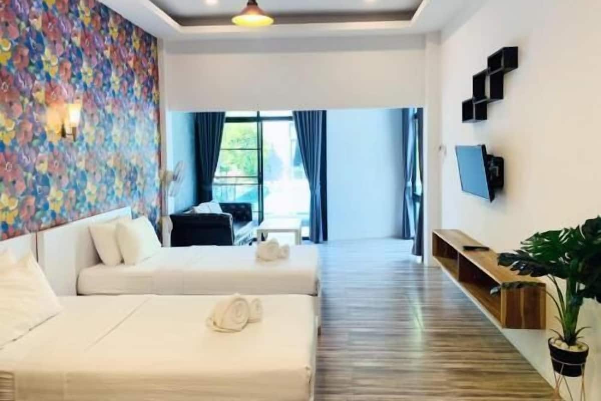 A hotel room with two beds, a colorful wall, a TV, and a view of the outdoors.