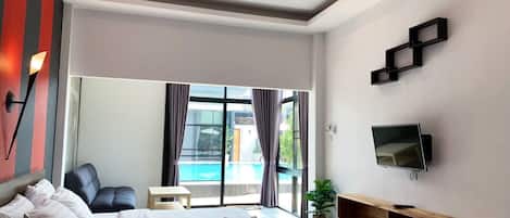 Habitación de hotel moderna con una cama grande, televisor, una mesita y vista a una piscina.