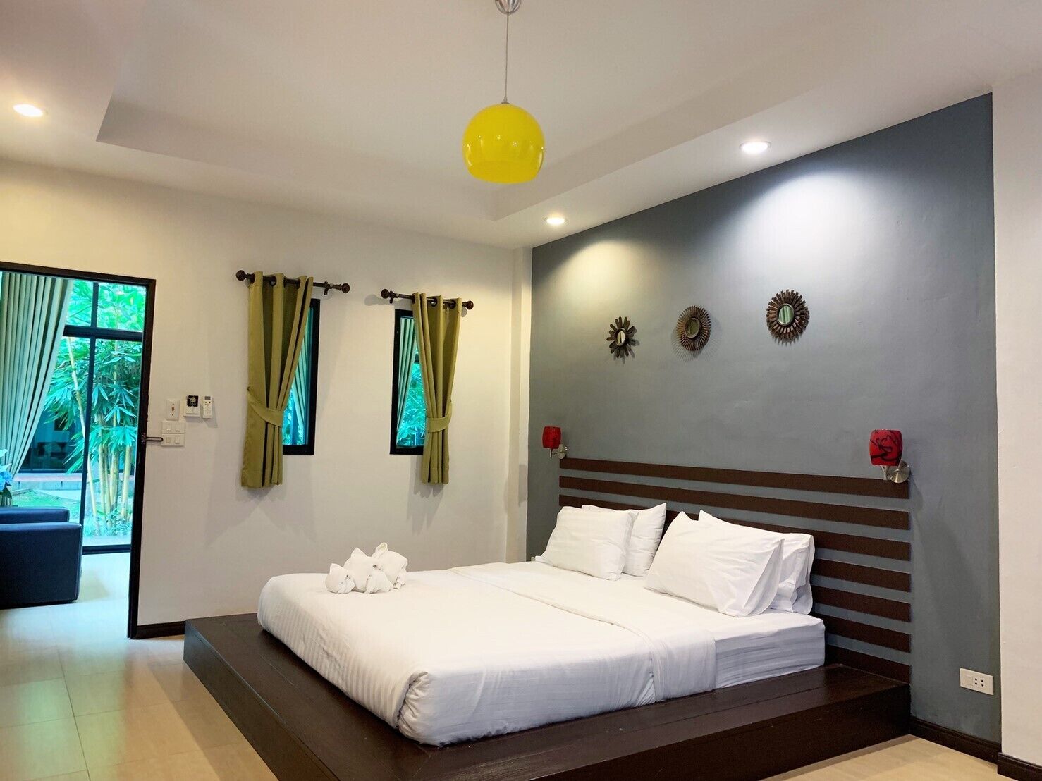 Un dormitorio moderno con una cama grande, vistas a zonas verdes por la ventana y una lámpara colgante amarilla.