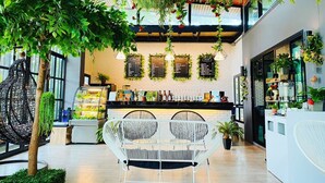 A modern cafe with a wooden ceiling, hanging plants, a black counter with menu boards, and white wicker chairs. - Baansuan Leelawadee Resort Nan (Nan)