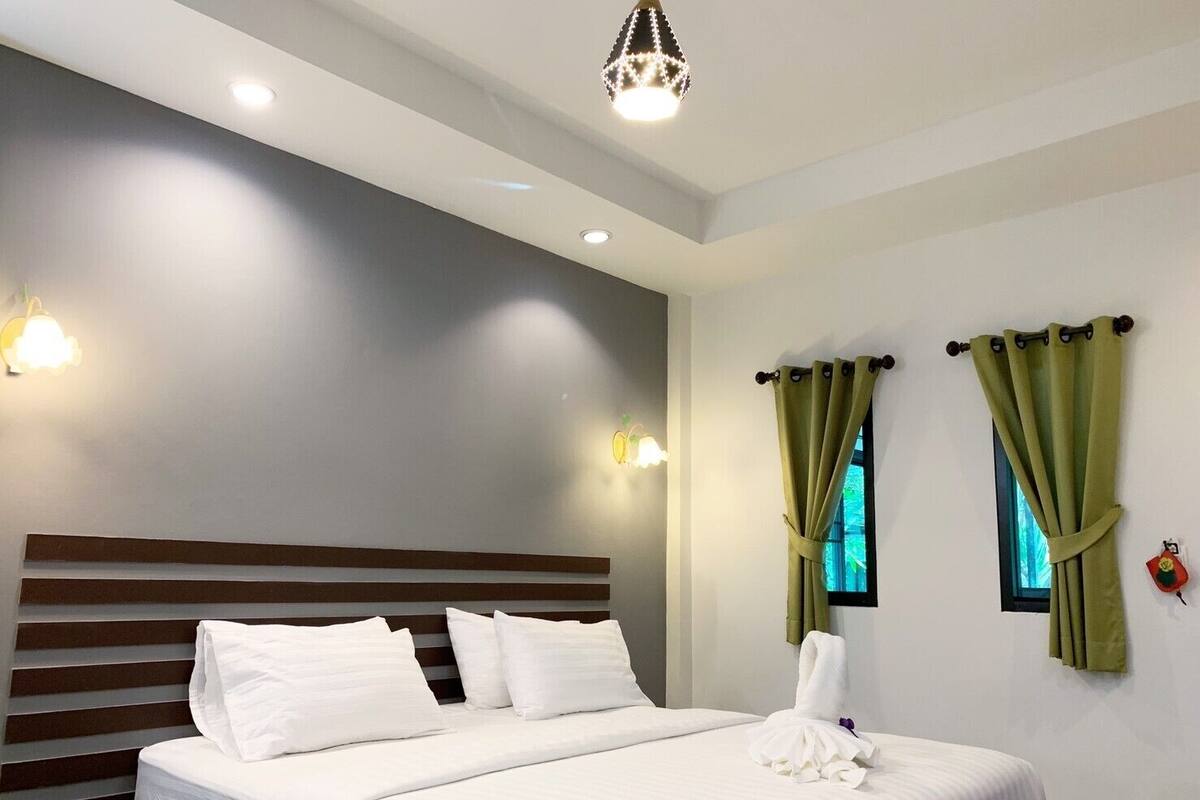 Une chambre d’hôtel avec un grand lit, deux lampes fixées au mur, un lustre et des rideaux verts.