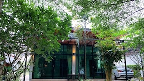 A modern building with a glass facade, surrounded by lush greenery and a pathway leading to the entrance. - Baansuan Leelawadee Resort Nan (Nan)