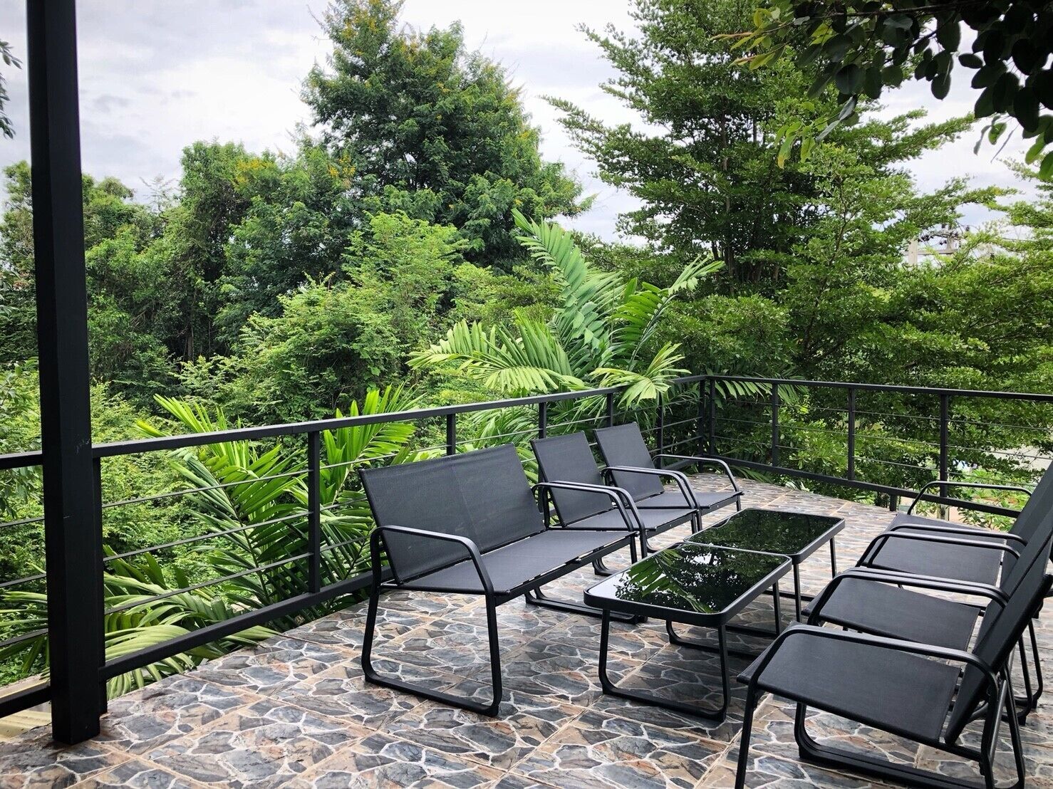 Una terraza con suelo de piedra, sillas de metal negro y una mesa de vidrio.
