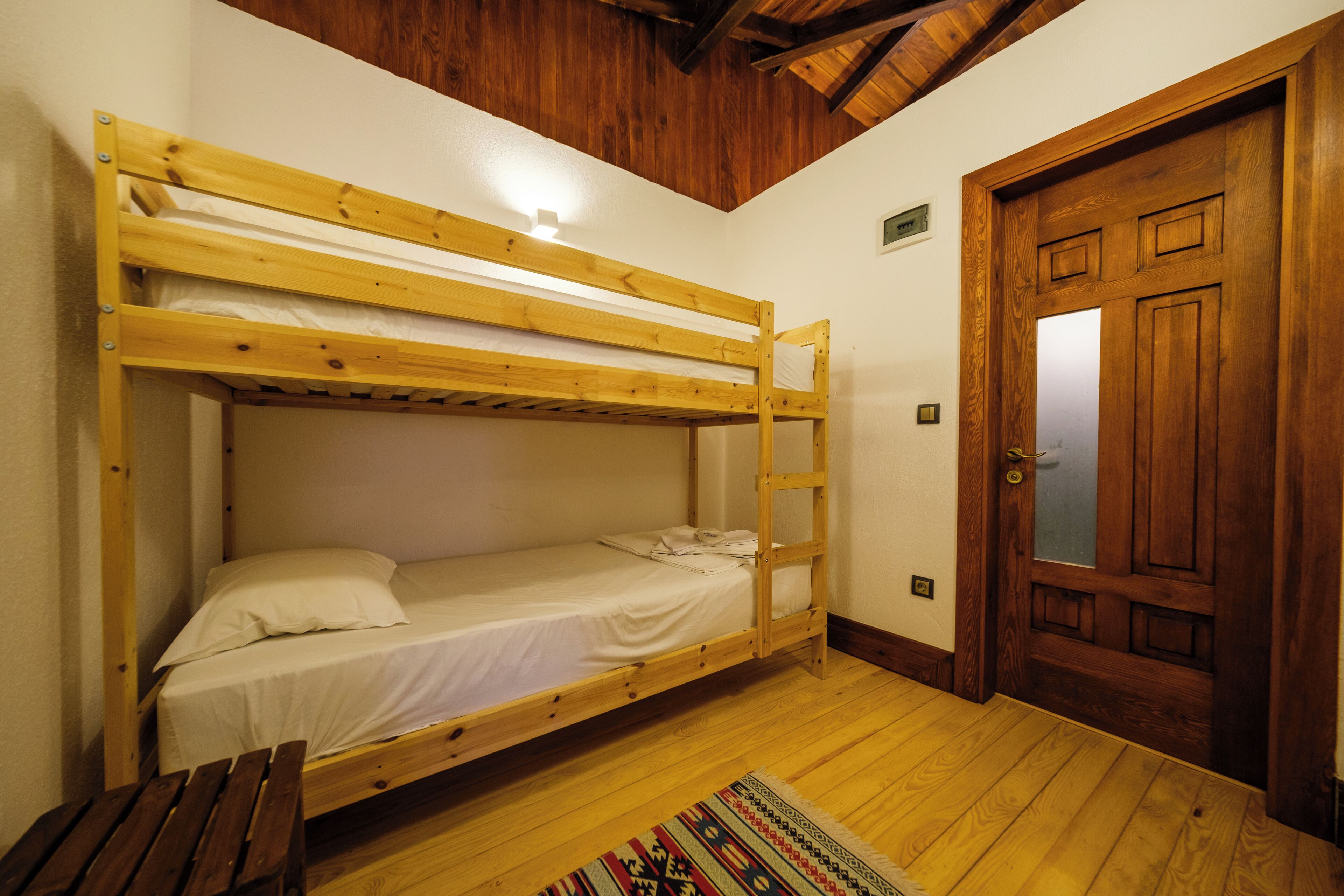 Habitación con literas, una puerta de madera y una pequeña alfombra en el suelo.