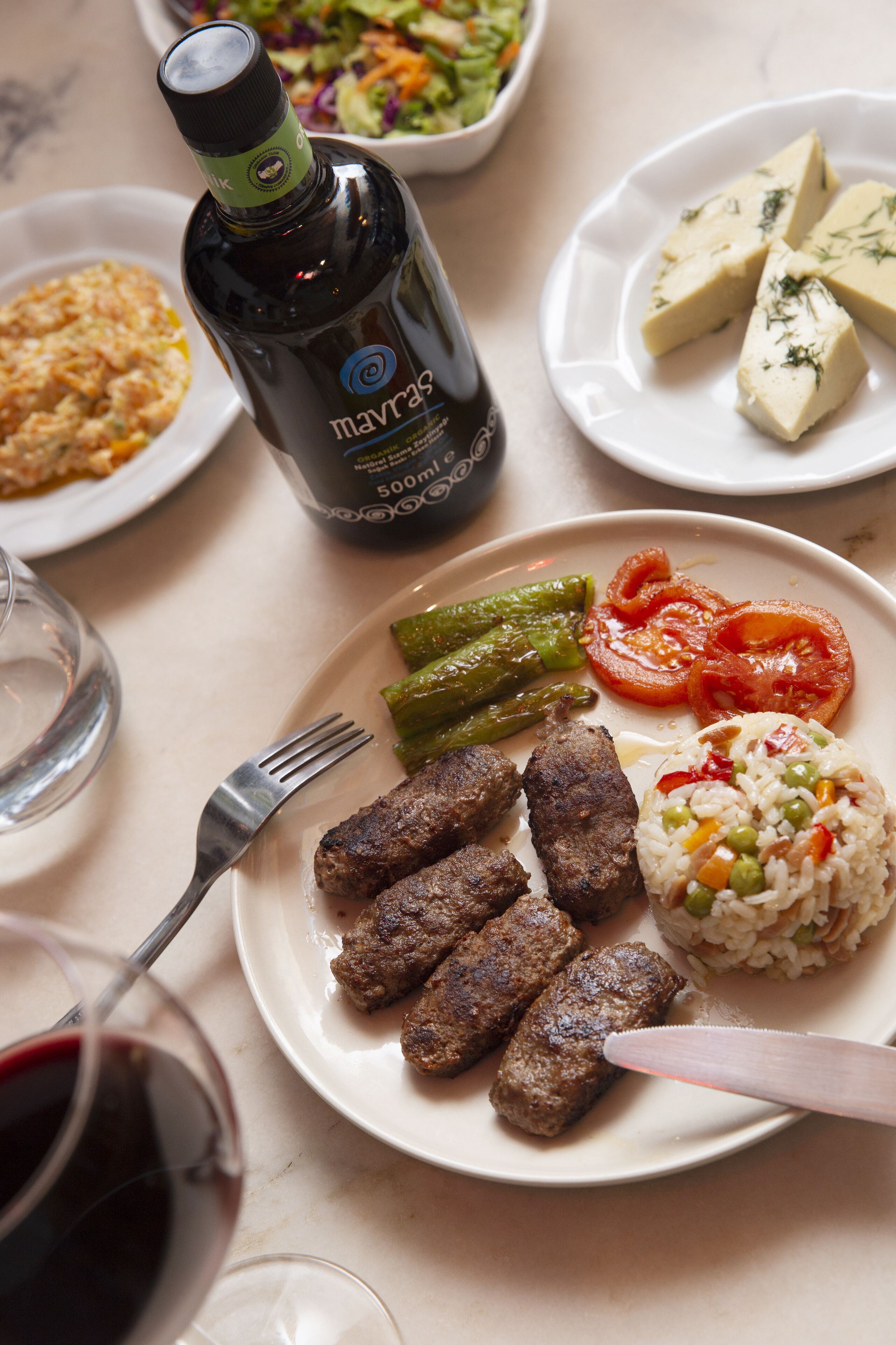A plate of food including sausages, rice, and vegetables, a bottle of drink, and a fork on a table.