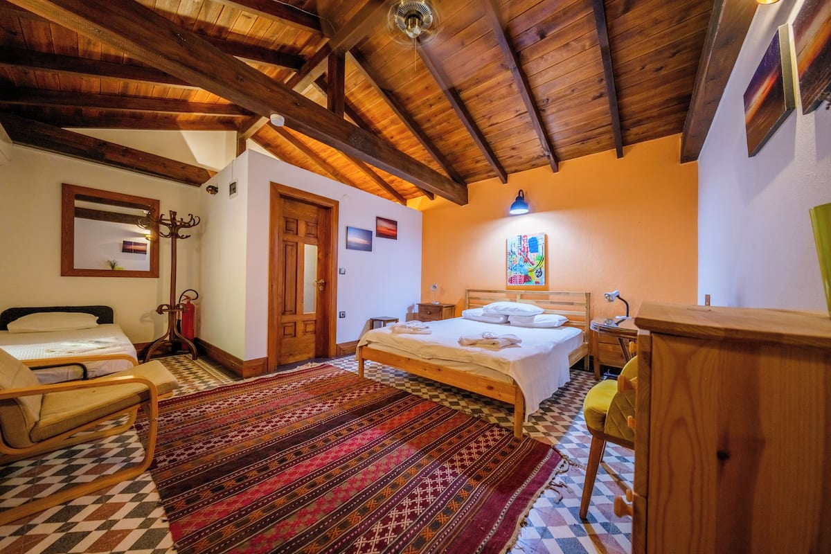 Un dormitorio con techo de madera, una cama, una silla, un escritorio y una alfombra estampada.