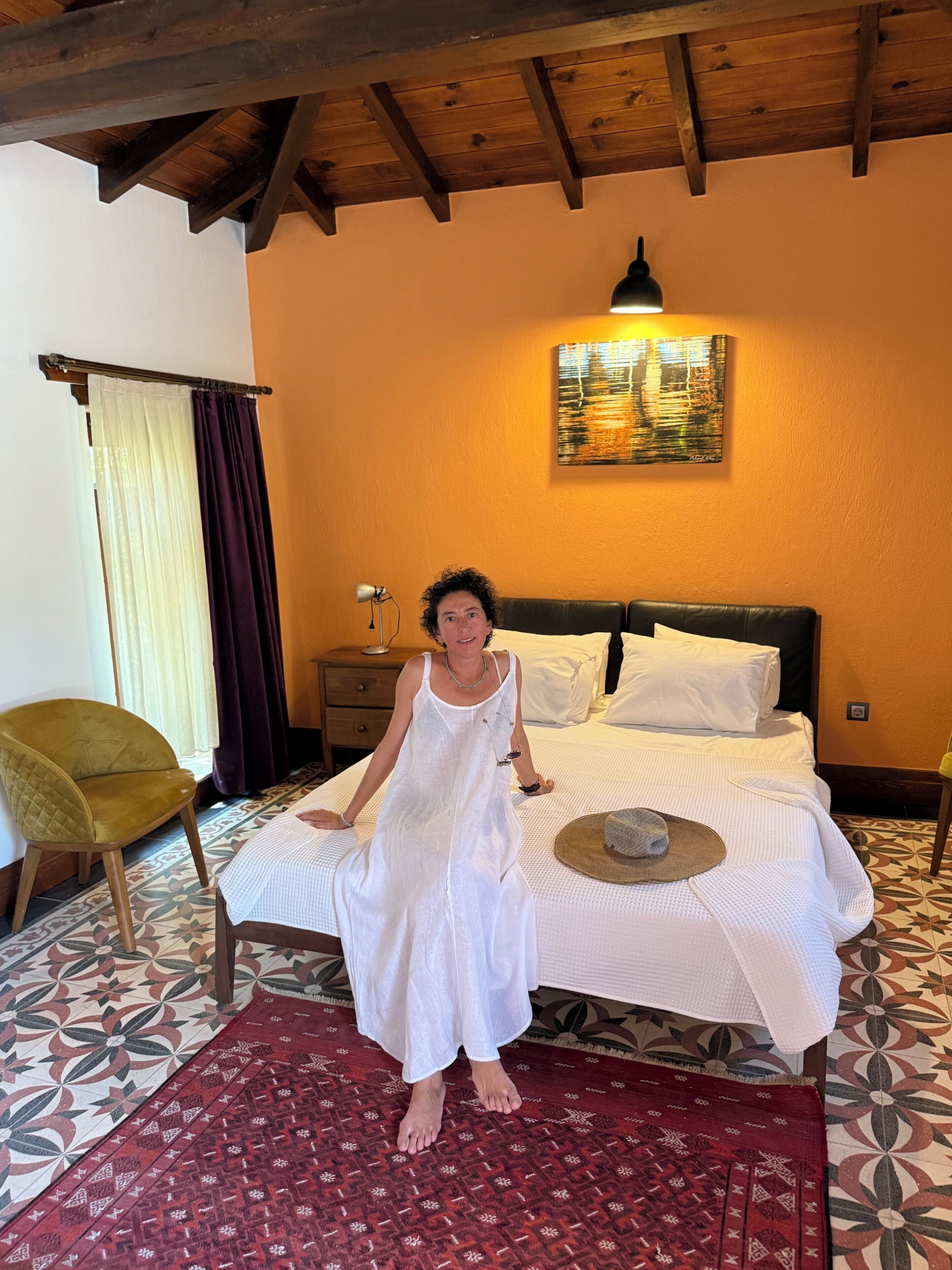 A room with a bed, a chair, a nightstand, a lamp, and a painting on the wall.