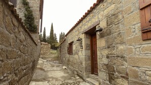 A narrow stone pathway between buildings with wooden shutters and stone walls. - Mavras Tas Odalar (Ayvacik)