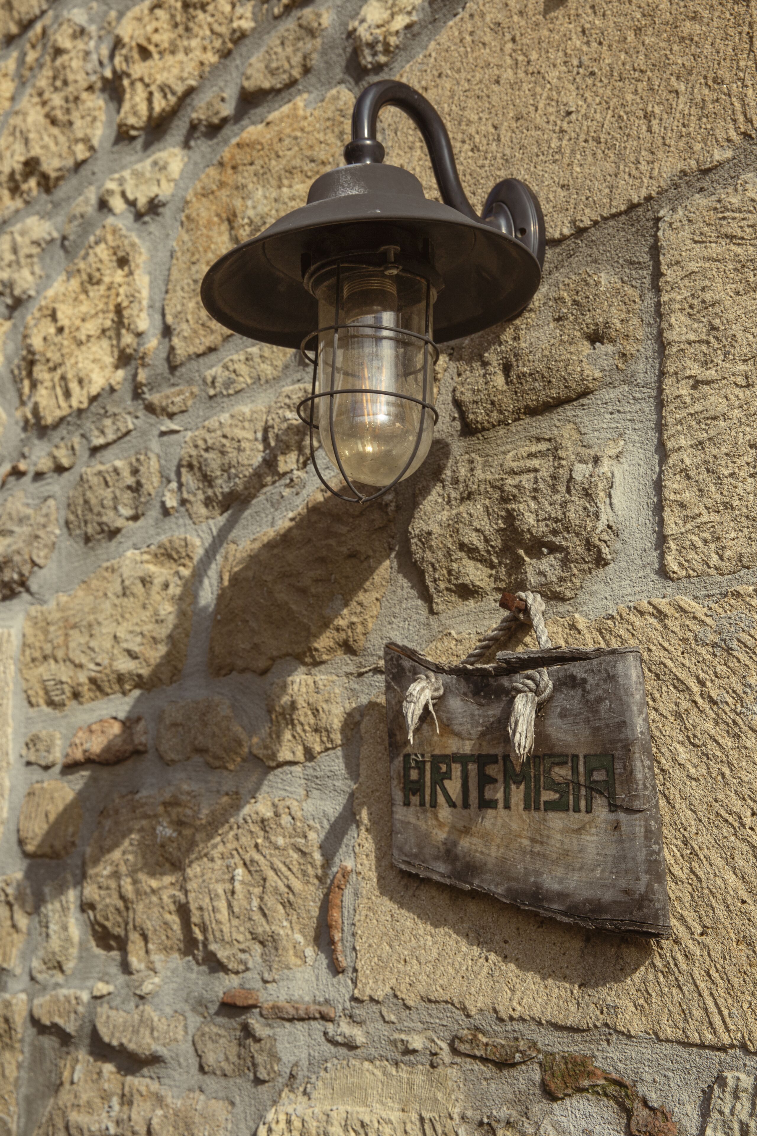A stone wall with a metal lantern and a wooden sign reading "ARTEMISIA".