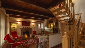 A cozy living room with a fireplace, wooden ceiling beams, a dining area, and a staircase. - Mavras Tas Odalar (Ayvacik)
