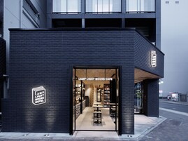 Un bâtiment moderne à la façade sombre et à l’entrée en verre. L’enseigne au-dessus de l’entrée indique : « LAMP LIGHT BOOKS CAFE ».