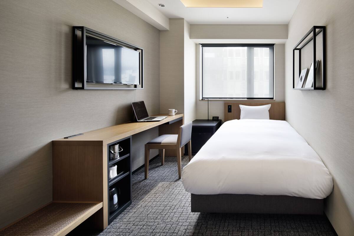 Una habitación de hotel moderna con cama, escritorio, silla y un ventanal grande.