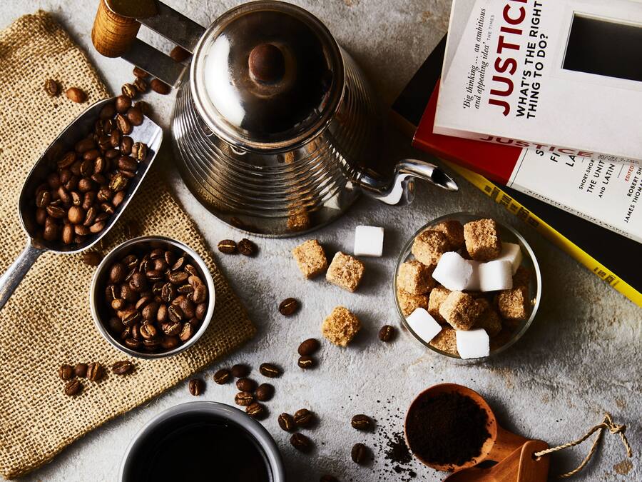 En kaffestation med en metallkanna, en sked med kaffebönor, en skål med sockerbitar och en bok med titeln ”RÄTTVISA”.
