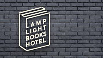 A neon sign on a brick wall that reads "LAMP LIGHT BOOKS HOTEL".